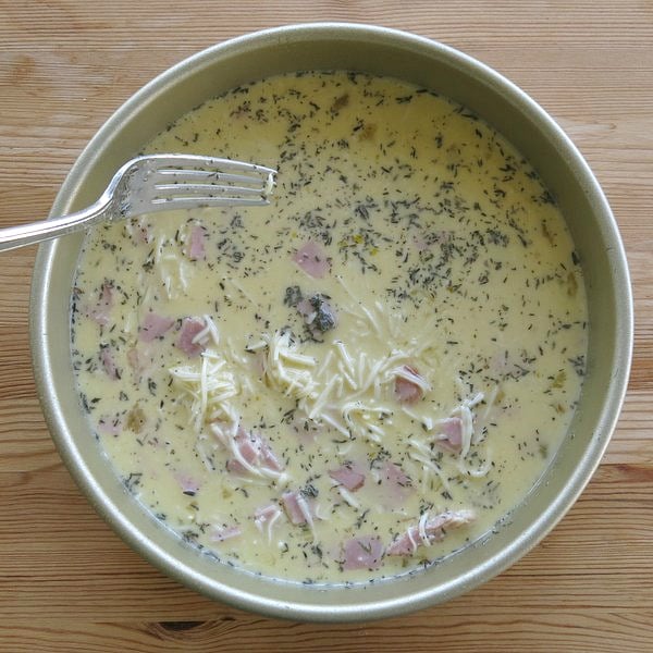 Crustless quiche filling in pan with fork to distribute ingredients.