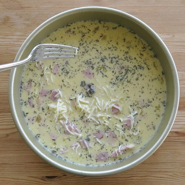 Crustless quiche filling in pan with fork to distribute ingredients