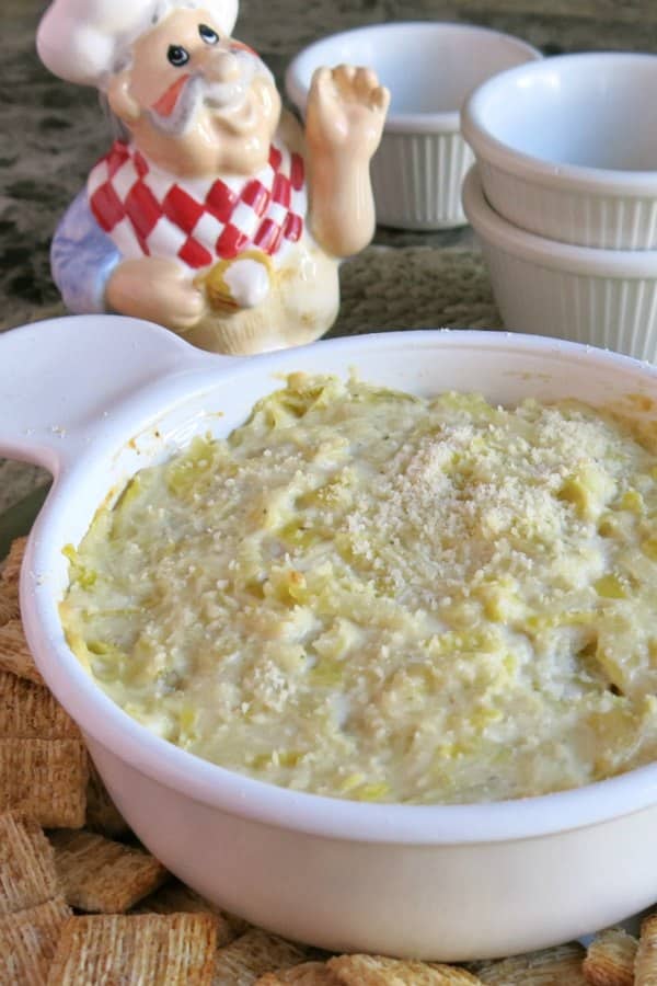 Hot artichoke dip in a bowl with stack of bowls next to it