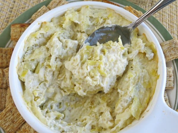 A spoon lifting warm artichoke dip out of bowl