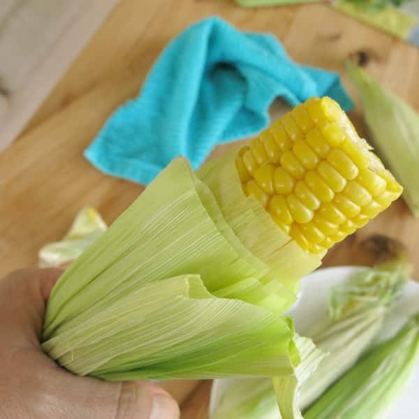 Microwave Corn on the Cob being pulled from husk with hand.