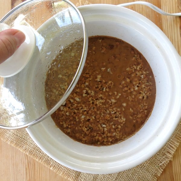 Uncooked Steel Cut Oatmeal in a CrockPot with lid partially removed.