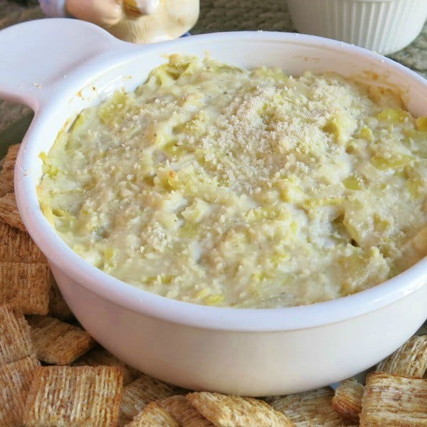 Warm artichoke dip in bowl surrounded by crackers