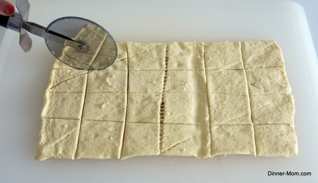 Pillsbury crescent roll dough being cut into squares with pizza cutter