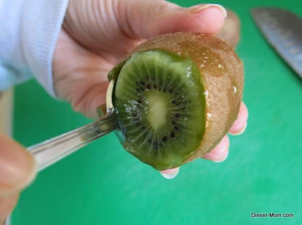 spoon inside skin of kiwi demonstrating trick for taking skin off