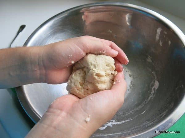 Hands kneading pretzel bites dough over a bowl.