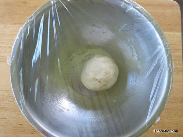 Dough for homemade pretzel bites in bowl covered with plastic wrap