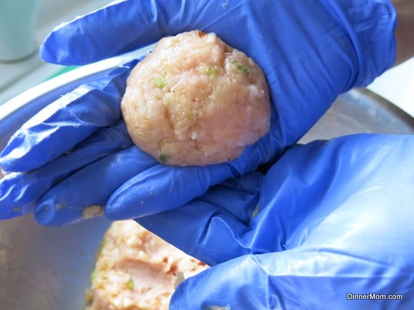 Hands in blue gloves holding a raw shaped turkey burger.