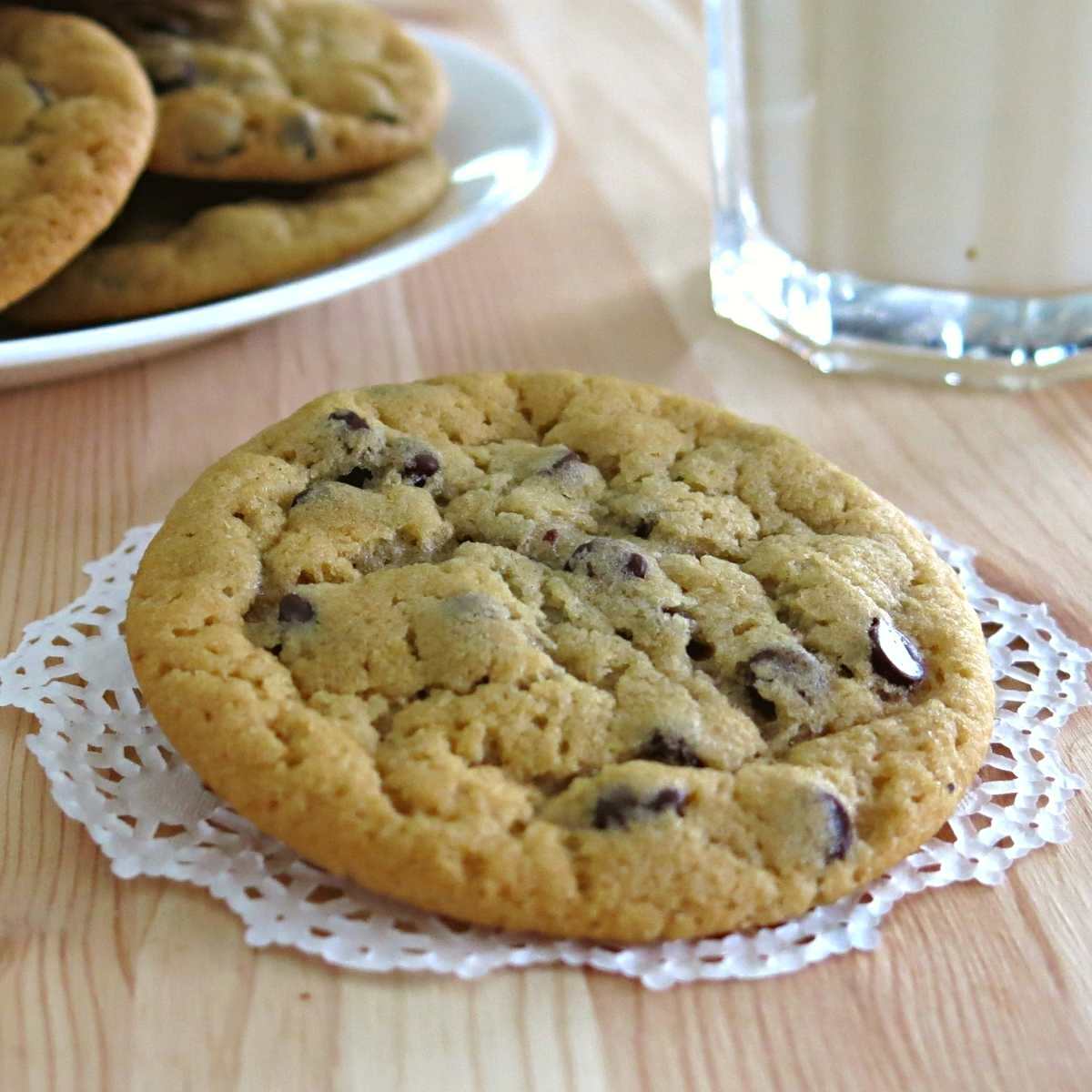 Plate with eggless chocolate chip cookies with plate of cookies and milk behind it.