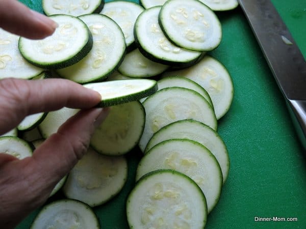 fingers holding Sliced Zucchini with lots of rounds on cutting board