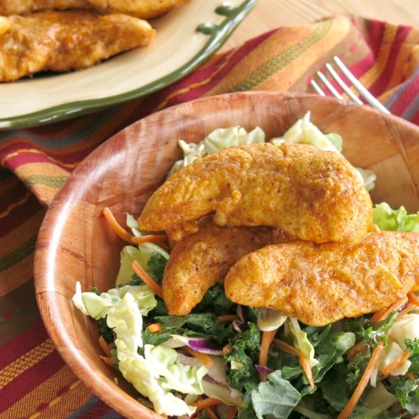 Parmesan Paprika Chicken tenders over salad greens in a bowl.