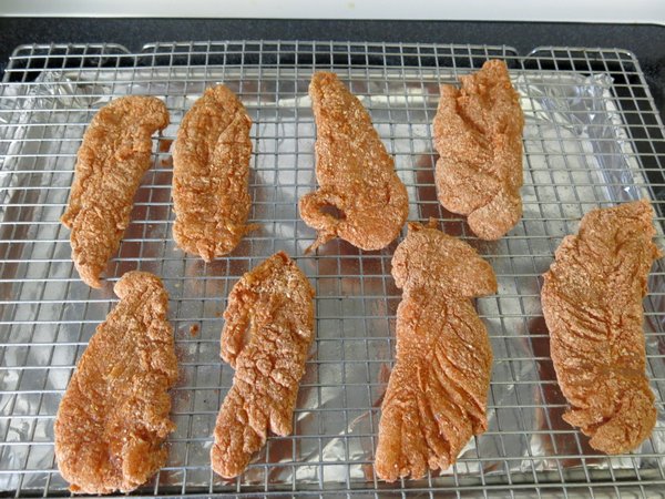 Chicken tenders coated with paprika Parmesan breading on baking rack.