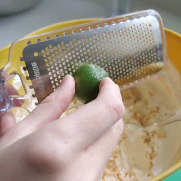 A key lime being zested into a large bowl with the rest of the key lime ingredients.