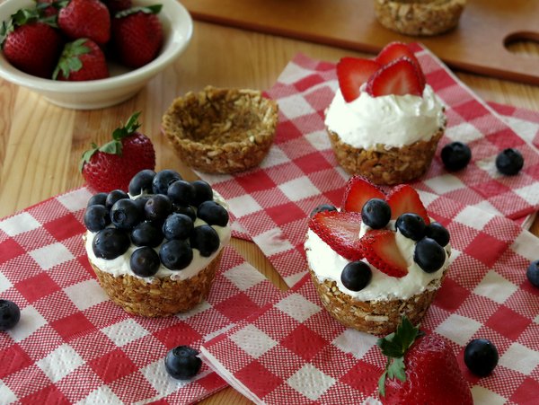 No-Bake Mini Cheesecakes topped with blueberries and strawberries, empty pretzel cups and bowls of berries