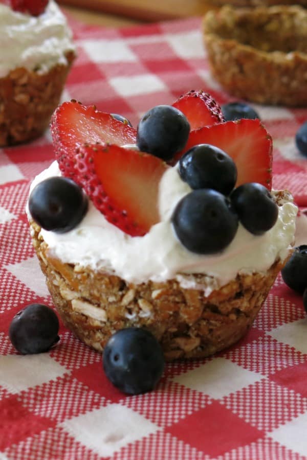 No-Bake Mini Cheesecakes topped with blueberries and strawberries in pretzel crust cup