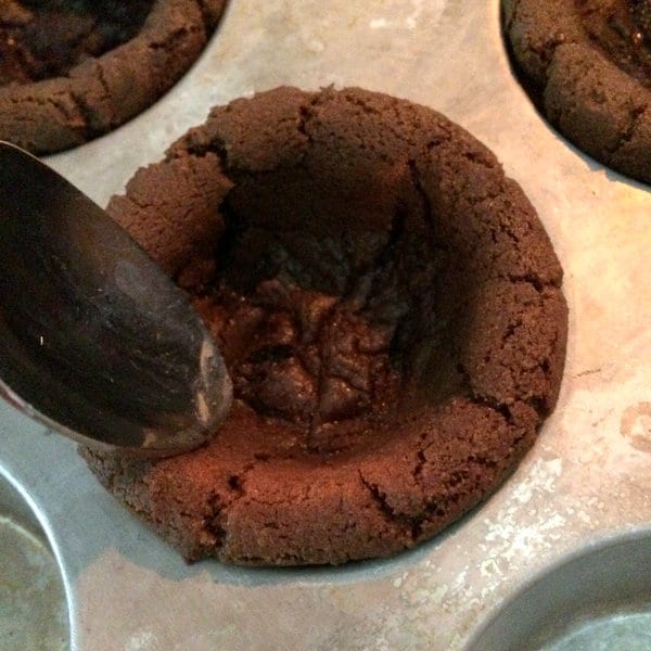 Spoon pressing down sides of partially cooked cookie cup.