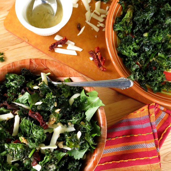Crispy Kale Chips in a bowl with almonds, sundried tomatoes and dressing beside it