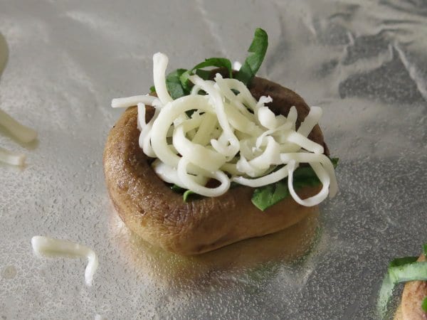 Mushroom pizza bite with spinach and mozzarella in side before being cooked.