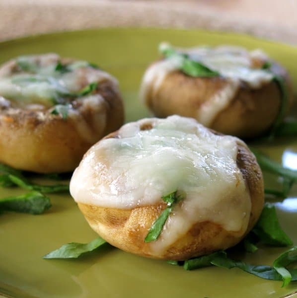 Three Pizza Stuffed Mushrooms on a plate on top of slivers of spinach