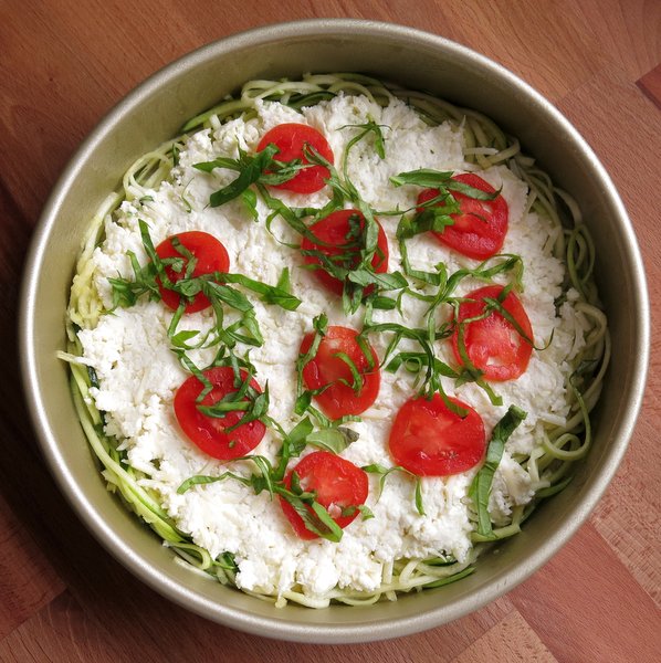 Sliced tomato and basil on uncooked zucchini pizza pie