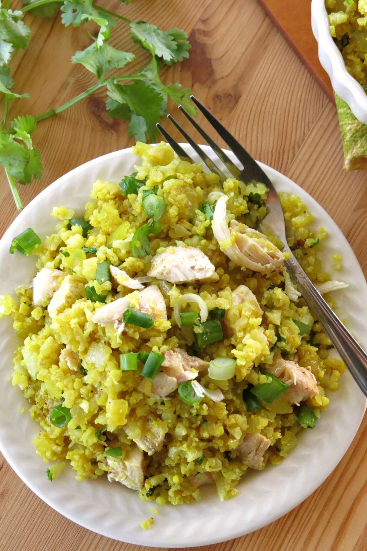 Curried cauliflower rice with pieces of chicken on top and cilantro in the background.