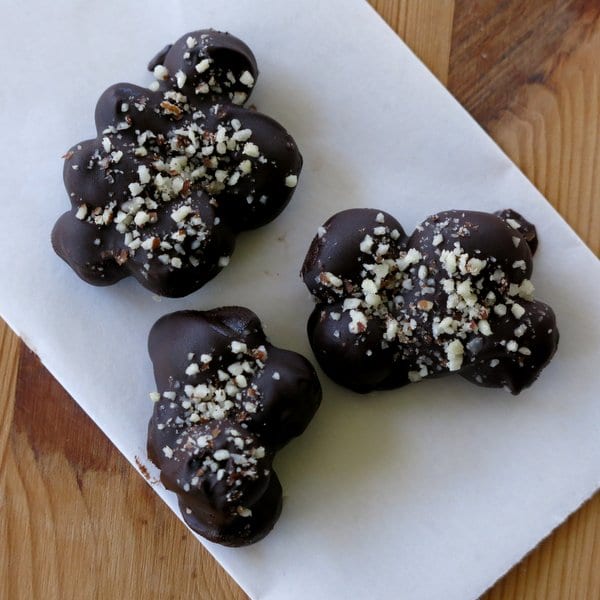 Three dark chocolate blueberry clusters on a piece of wax paper.