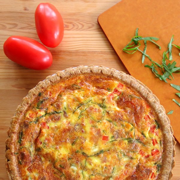 Tomato Bacon Quiche next to plum tomatoes and basil.