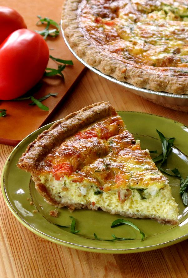 Bacon and Tomato Quiche Recipe on plate with plum tomatoes in background.