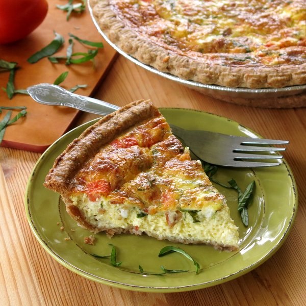 Slice of Tomato Bacon Quiche on plate next to pan with the rest of the quiche.