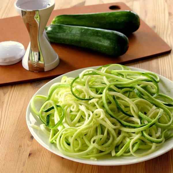 Spiralized Zucchini Noodles with zucchini and hand held spiralizer in the background