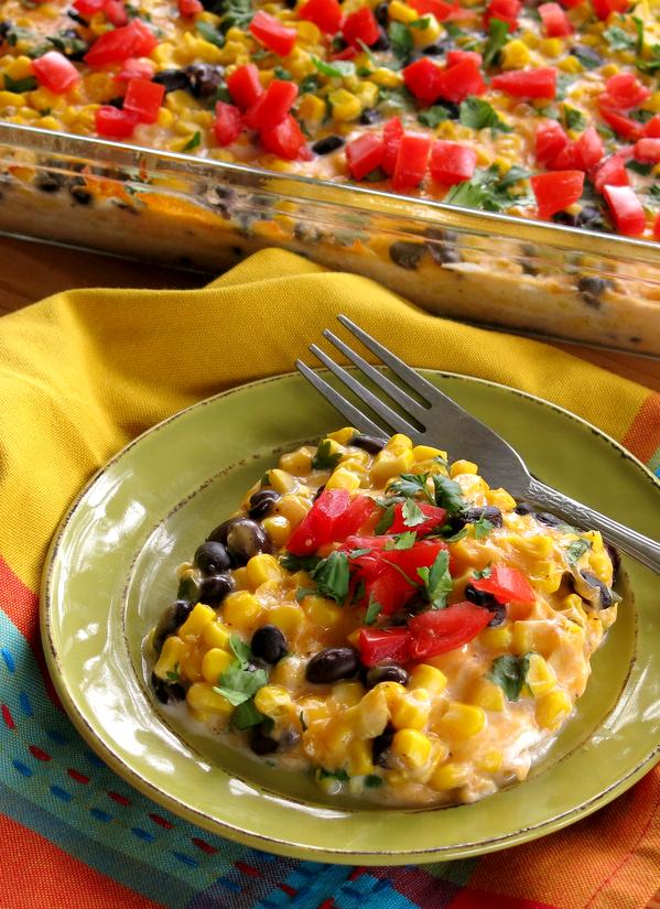 Serving of Tex Mex Cheddar Corn Casserole on plate with casserole dish behind it