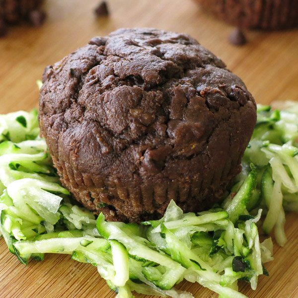 Chocolate zucchini muffin on top of a pile of shredded zucchini on a cutting board.