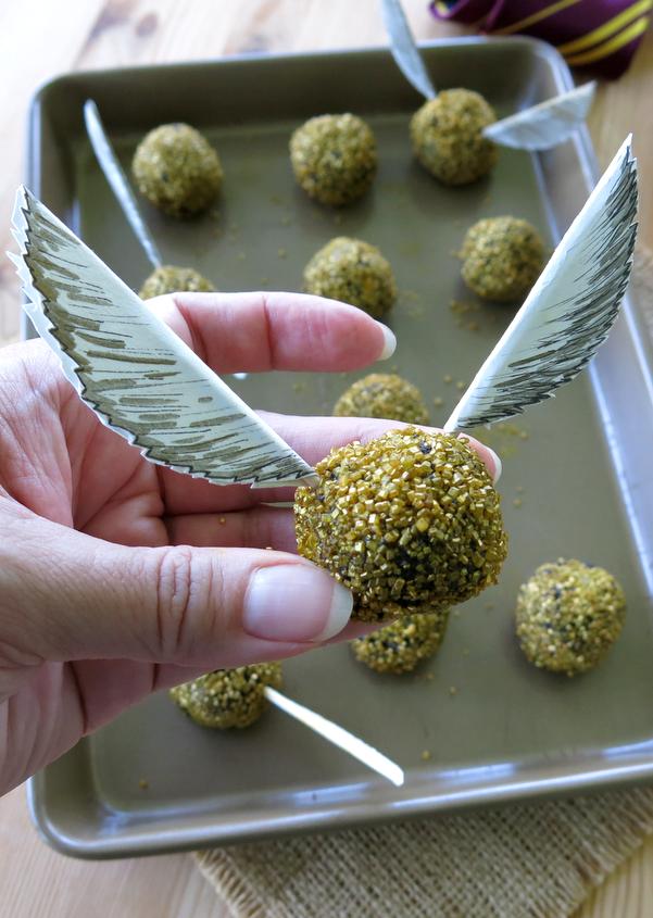 Hand holding an edible Harry Potter Golden Snitch Truffle with paper wings.