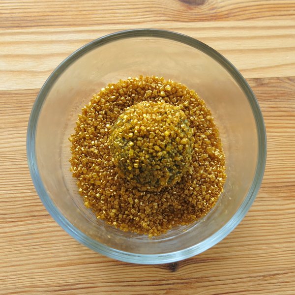 Oreo balls dipped in bowl of gold sprinkles.