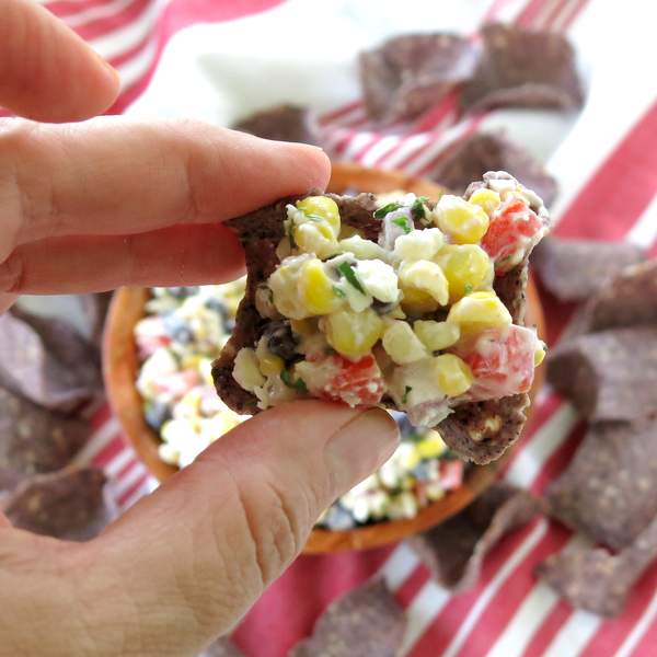 Hand holding Mexican street corn dip on a chip