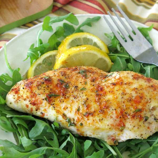 Baked Lemon Pepper Chicken breast on a plate with a fork and lemons