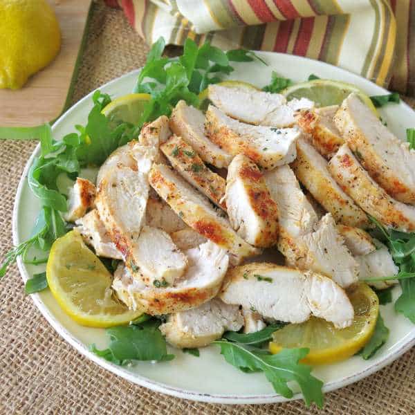 Healthy Baked Lemon Pepper Chicken sliced into strips on a plate of greens with lemons