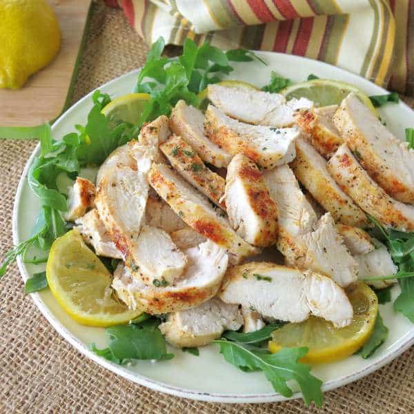 Healthy Baked Lemon Pepper Chicken sliced into strips on a plate of greens with lemons.