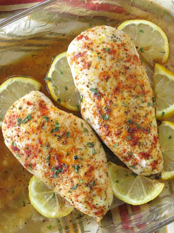 Two Oven Baked Lemon Pepper Chicken breasts in a baking dish with lemons around it