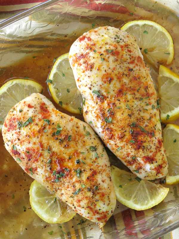 Two Oven Baked Lemon Pepper Chicken breasts in a baking dish with lemons around it.