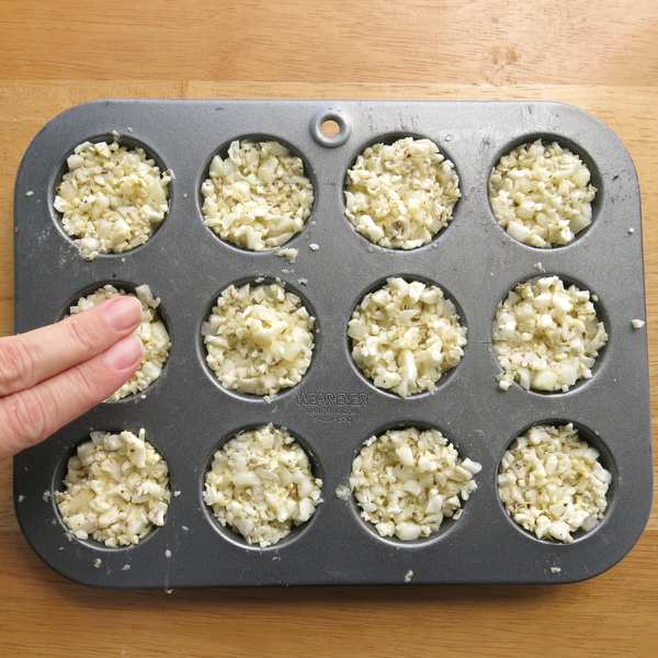 Two fingers pressing down on cauliflower egg muffins to compact the mixture