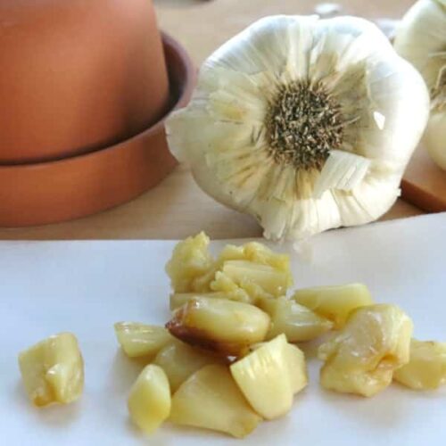 Roasted garlic cloves in a pile in front of bulb of garlic