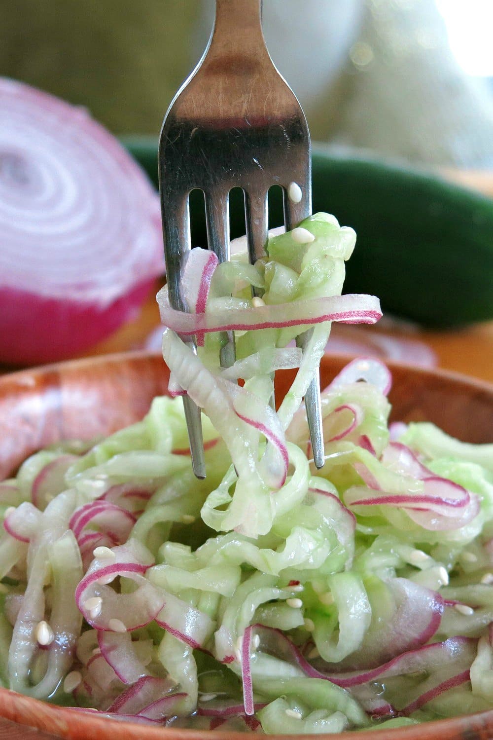 Fork pulling up spiralized cucumber and onion from salad.