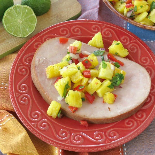 Slice of ham topped with pineapple salsa on a plate.