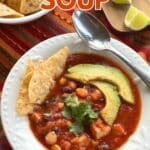 Bowl of chicken tortilla soup with hominy, black beans, and corn topped with sliced avocado and 3 tortilla chips.