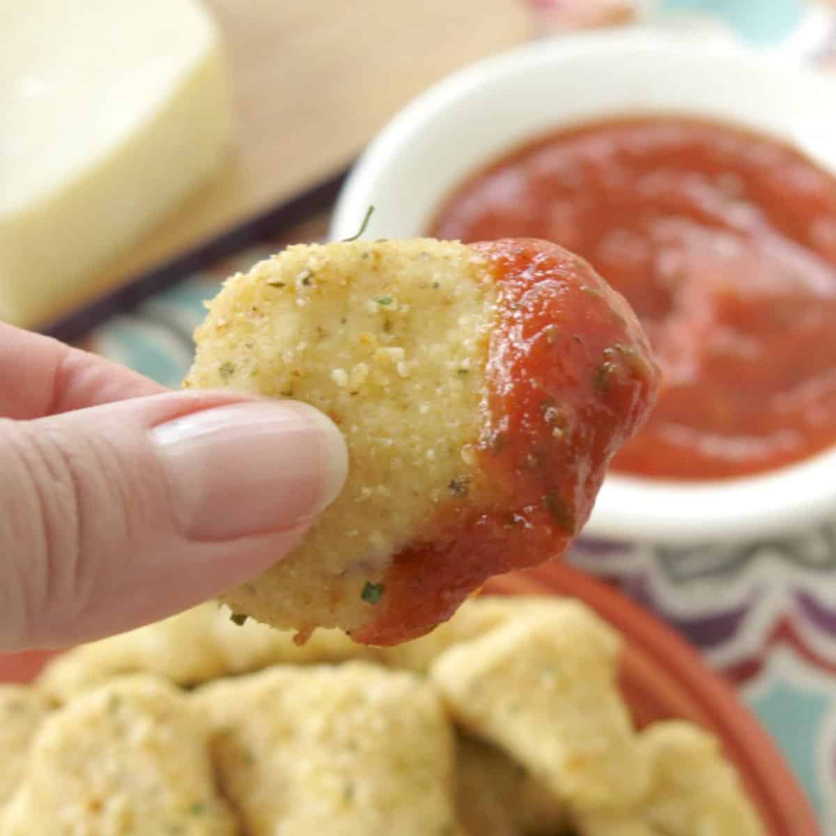 Fingers holding up a Garlic Parmesan chicken bite that has been dipped in marinara.