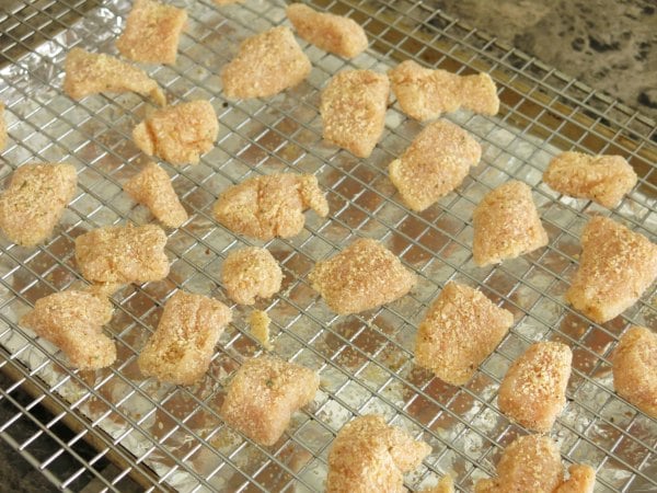 Uncooked garlic parmesan chicken bites on a rack over a baking sheet.