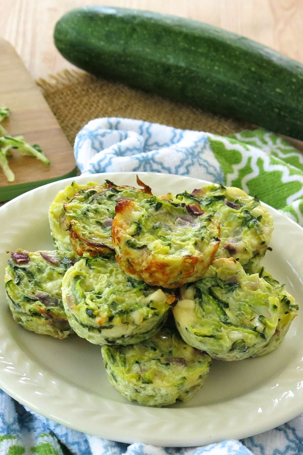 Stack of healthy zucchini egg muffins on plate with a whole zucchini behind it.