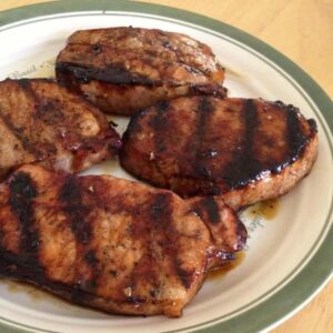 4 pork chops with molasses marinade on a plate.