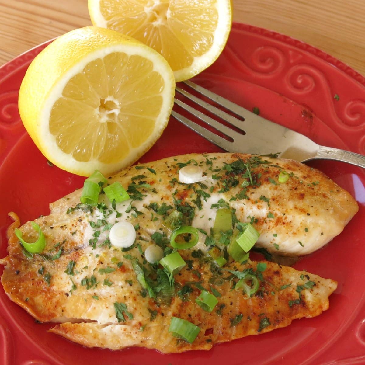 Baked lemon pepper tilapia on plate with a lemon halves and a fork.